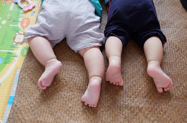 Two babies lie side by side on play mats.
