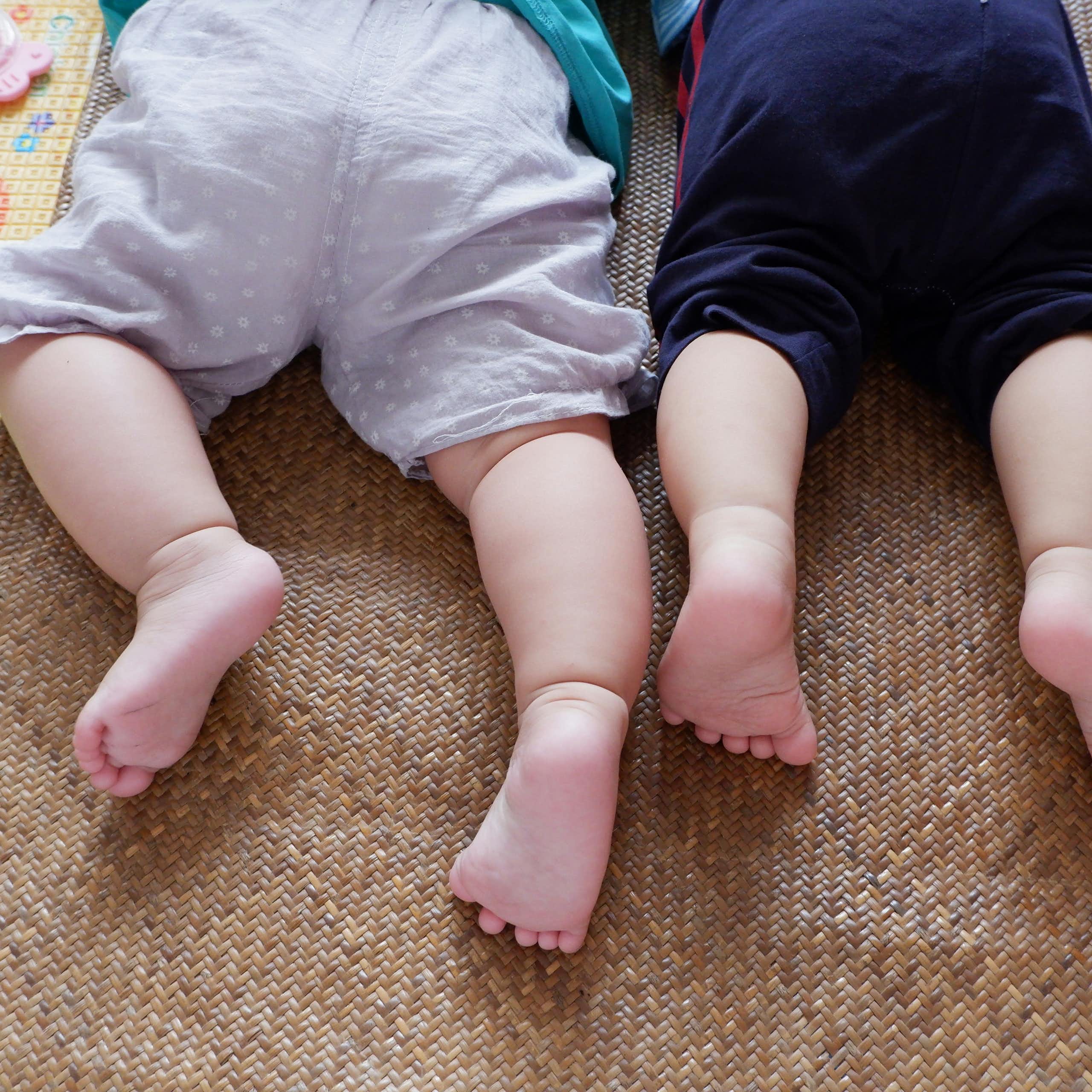 Two babies lie side by side on play mats.