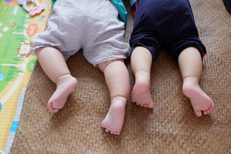 Two babies lie side by side on play mats.