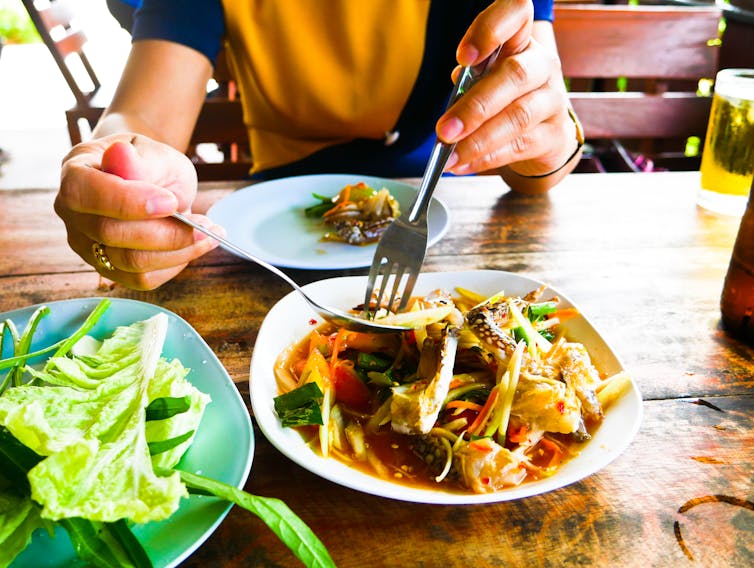 A woman spoons spicy Thai food onto her plate.