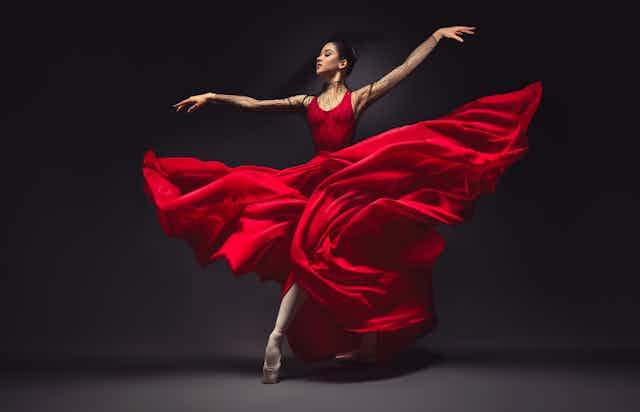 Young graceful woman ballet dancer, dressed in professional outfit, shoes and red weightless skirt is demonstrating dancing skill.