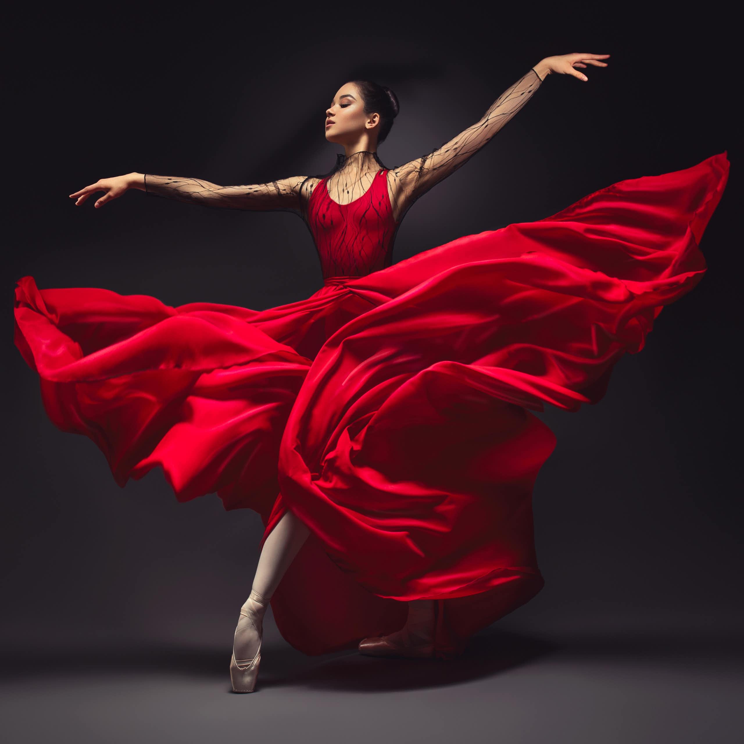 Young graceful woman ballet dancer, dressed in professional outfit, shoes and red weightless skirt is demonstrating dancing skill.