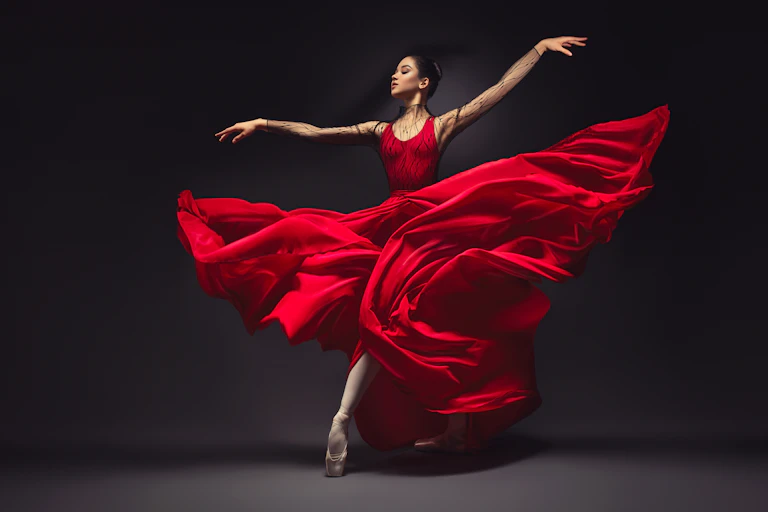 Young graceful woman ballet dancer, dressed in professional outfit, shoes and red weightless skirt is demonstrating dancing skill.