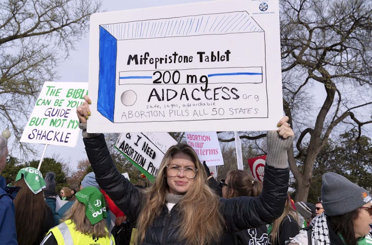 a woman holds a sign supporting access to abortion pills at a protest rally