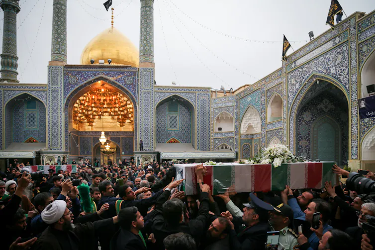 Mourners carry a coffin draped in white, red and green past a shrine.