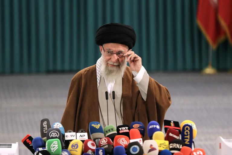 Ali Khamenei dressed in a brown robe and adjusting his glasses.