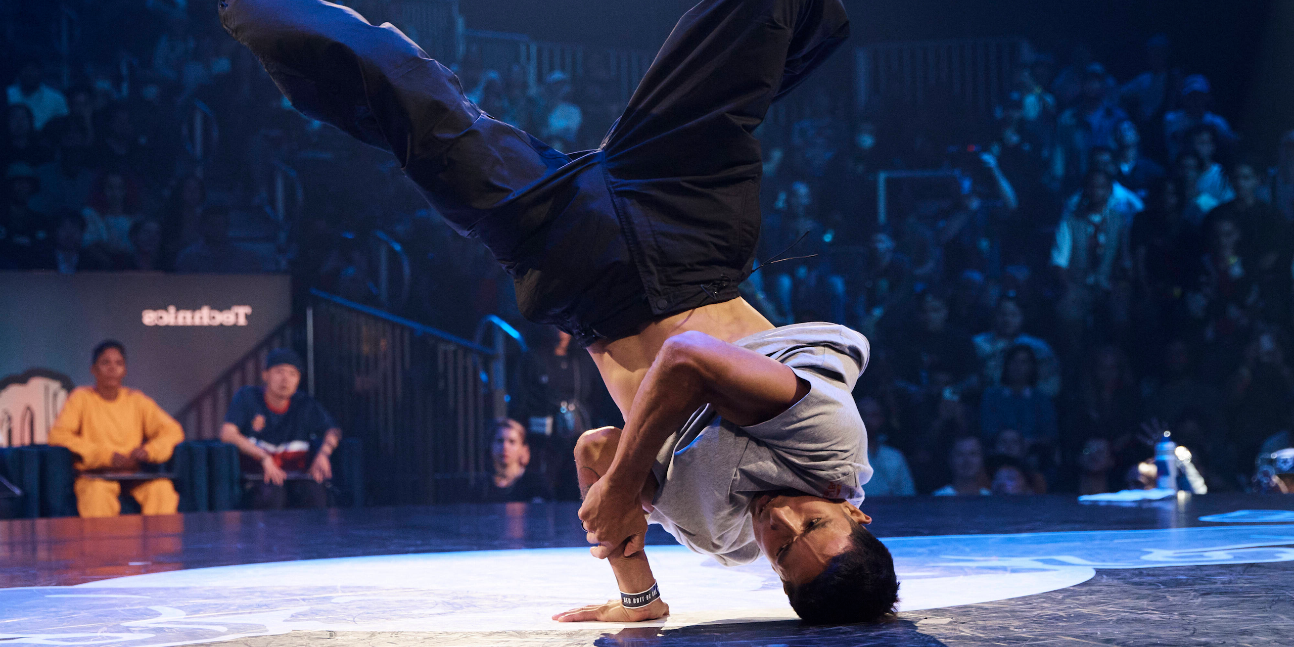 A break dancer does a spin with his head and hand in contact with the floor and his legs in the air. 