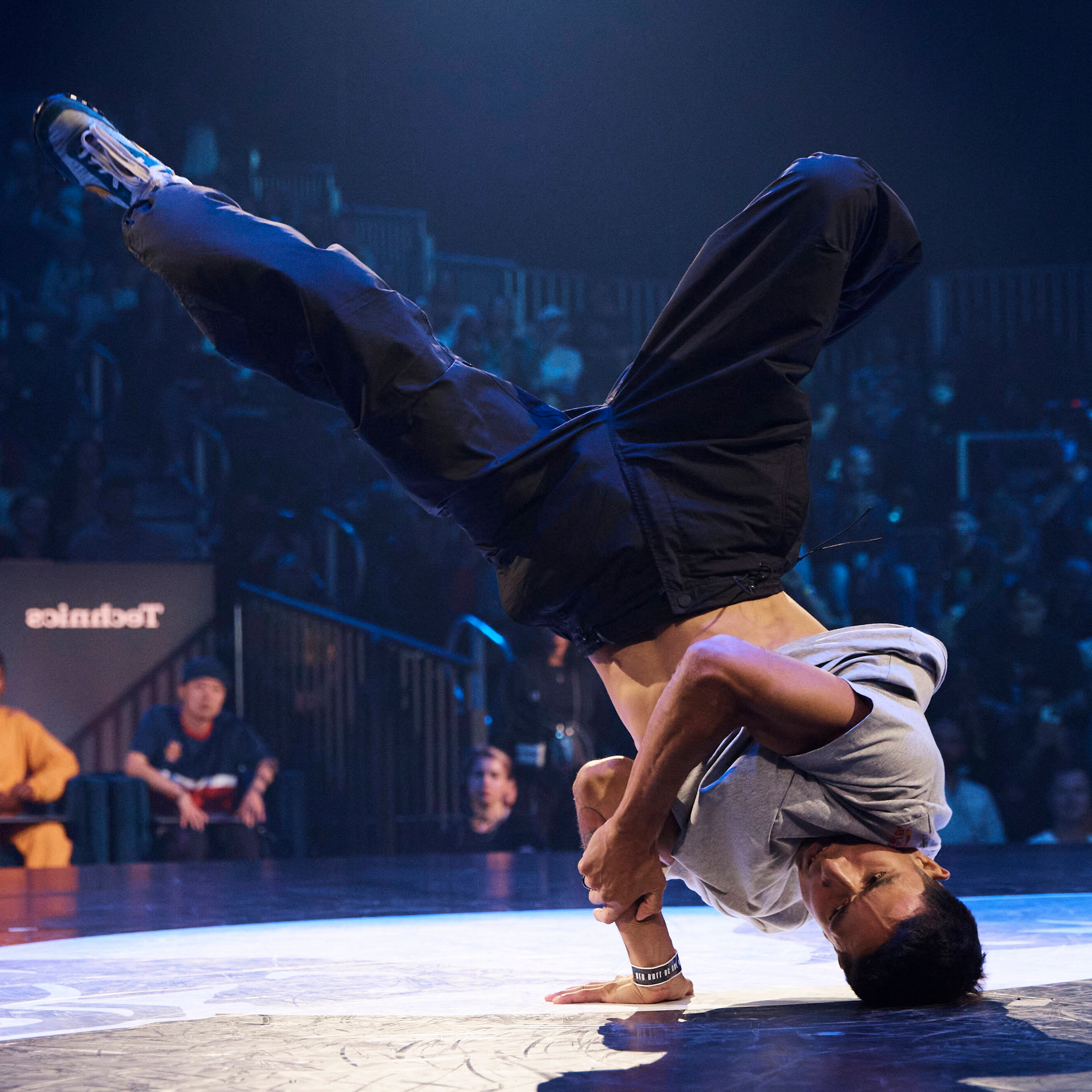 A break dancer does a spin with his head and hand in contact with the floor and his legs in the air. 