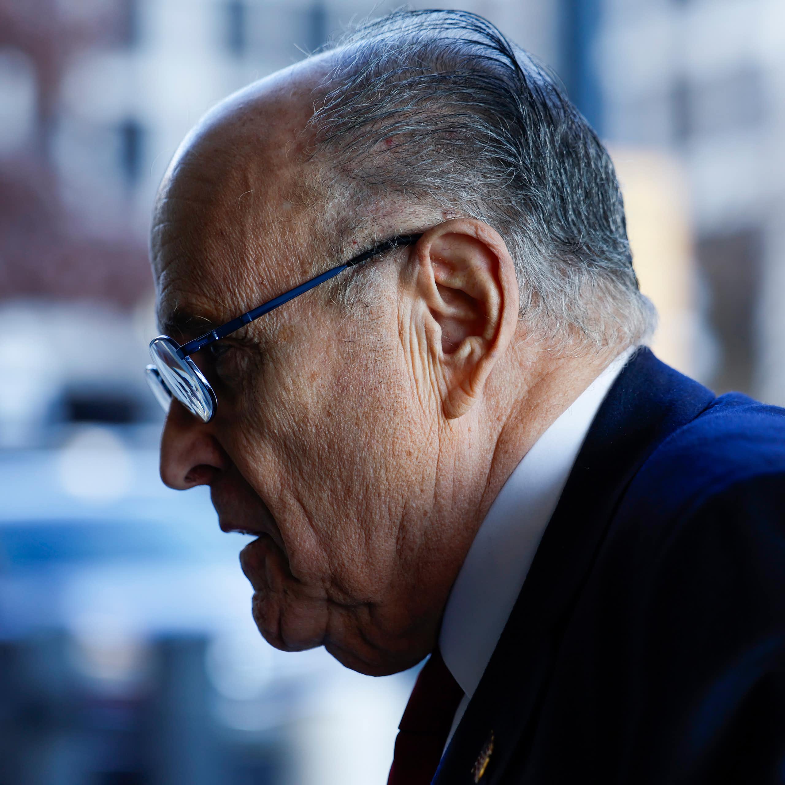 A balding man with glasses in a blue jacket, seen in profile.