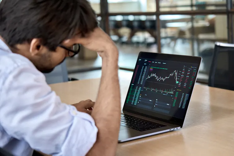Rear shot of a man resting his head against his hand as he looks at graphs displayed on a computer screen.