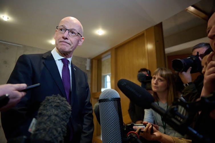 John Swinney falando com a mídia.
