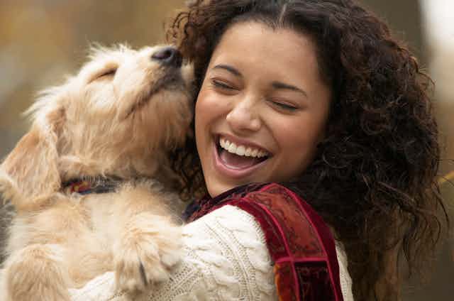 Uma jovem mulher ri enquanto segura seu cachorro perto do rosto.