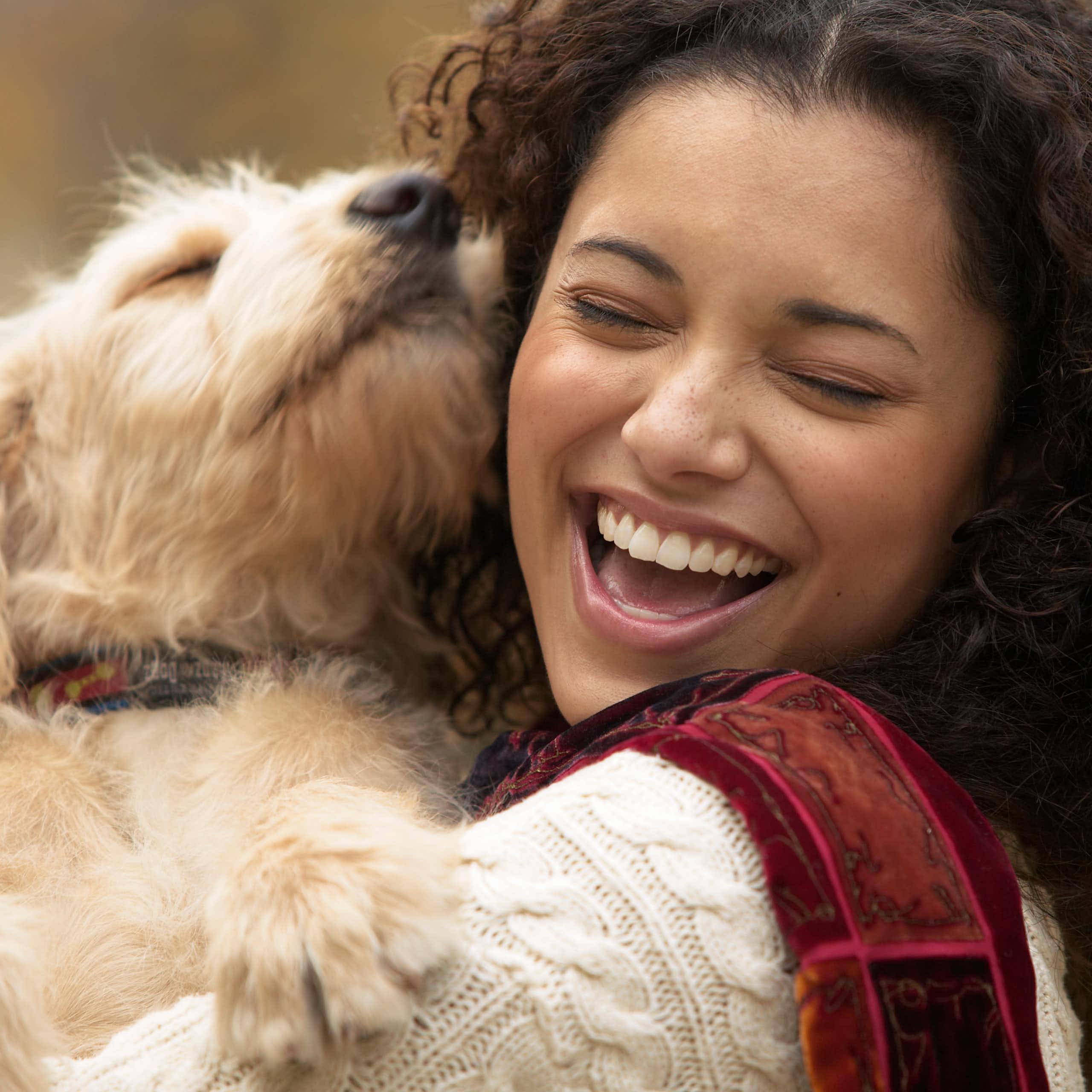 Uma jovem mulher ri enquanto segura seu cachorro perto do rosto.