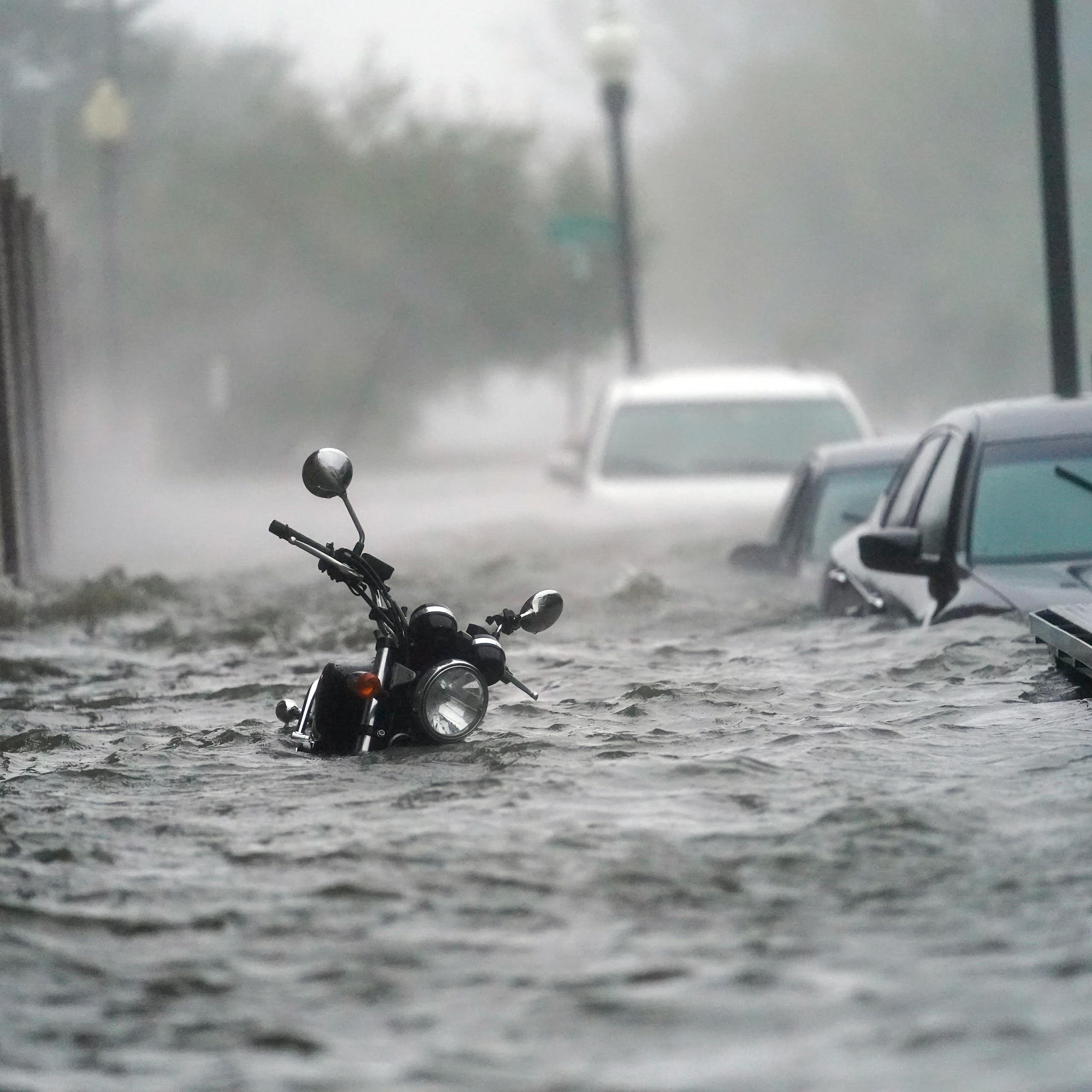 A flooded street during a hurricane with water up to the handle bars on a motorcycle and over the doors on cars parked along a street in Pensacola in 2020.