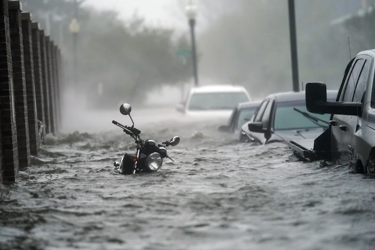 A flooded street during a hurricane with water up to the handle bars on a motorcycle and over the doors on cars parked along a street in Pensacola in 2020.
