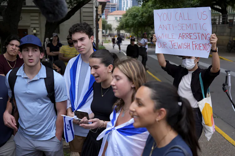 A Pro-Palestinian protester holds up a sign behind Jewish students.