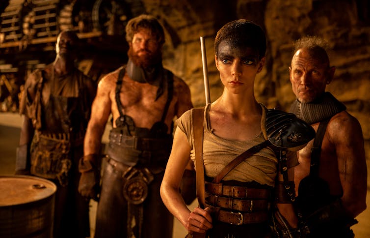 Production image. Furiosa and two men in yellow light.
