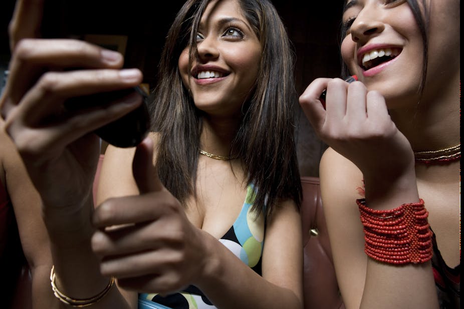 Deux jeunes femmes se maquillent en tenant un miroir. Elles sourient. à aller à une fête.