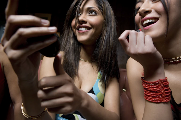 Deux jeunes femmes se maquillent en tenant un miroir. Elles sourient. à aller à une fête.
