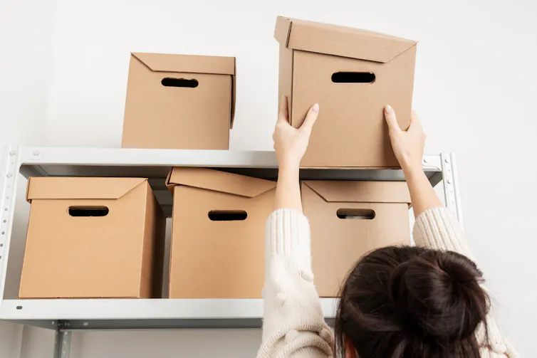 A woman gets a box down from a shelf.