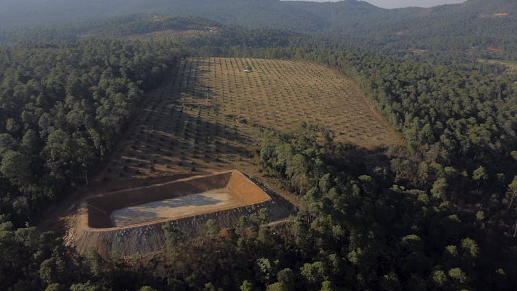 A large rectangular excavation in a clearing surrounded by forests