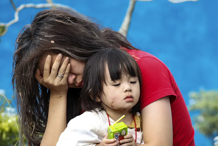 A woman holds her head in her hand while she holds her toddler.