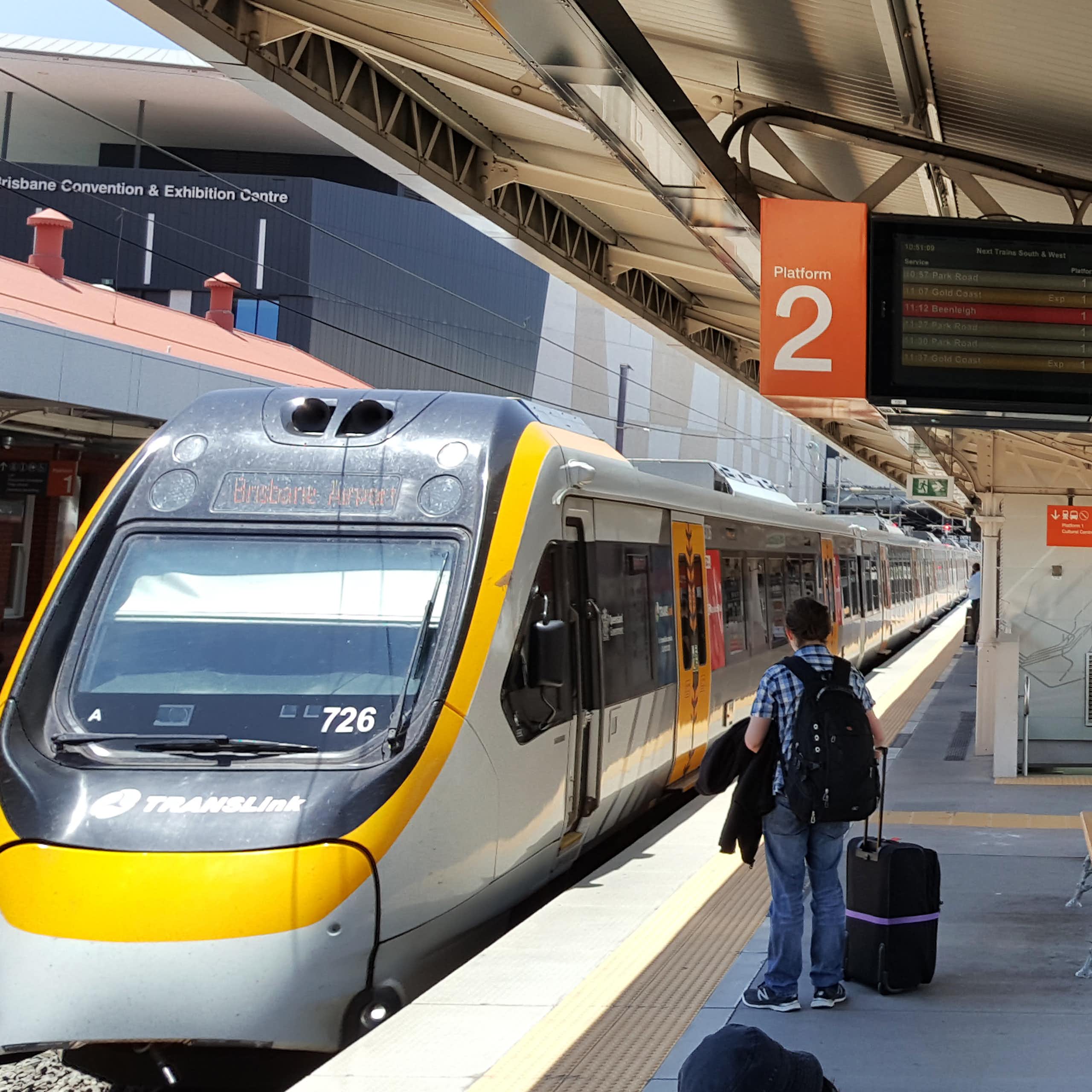 Train pulls into South Brisbane station, man seen waiting on platform with suitcase