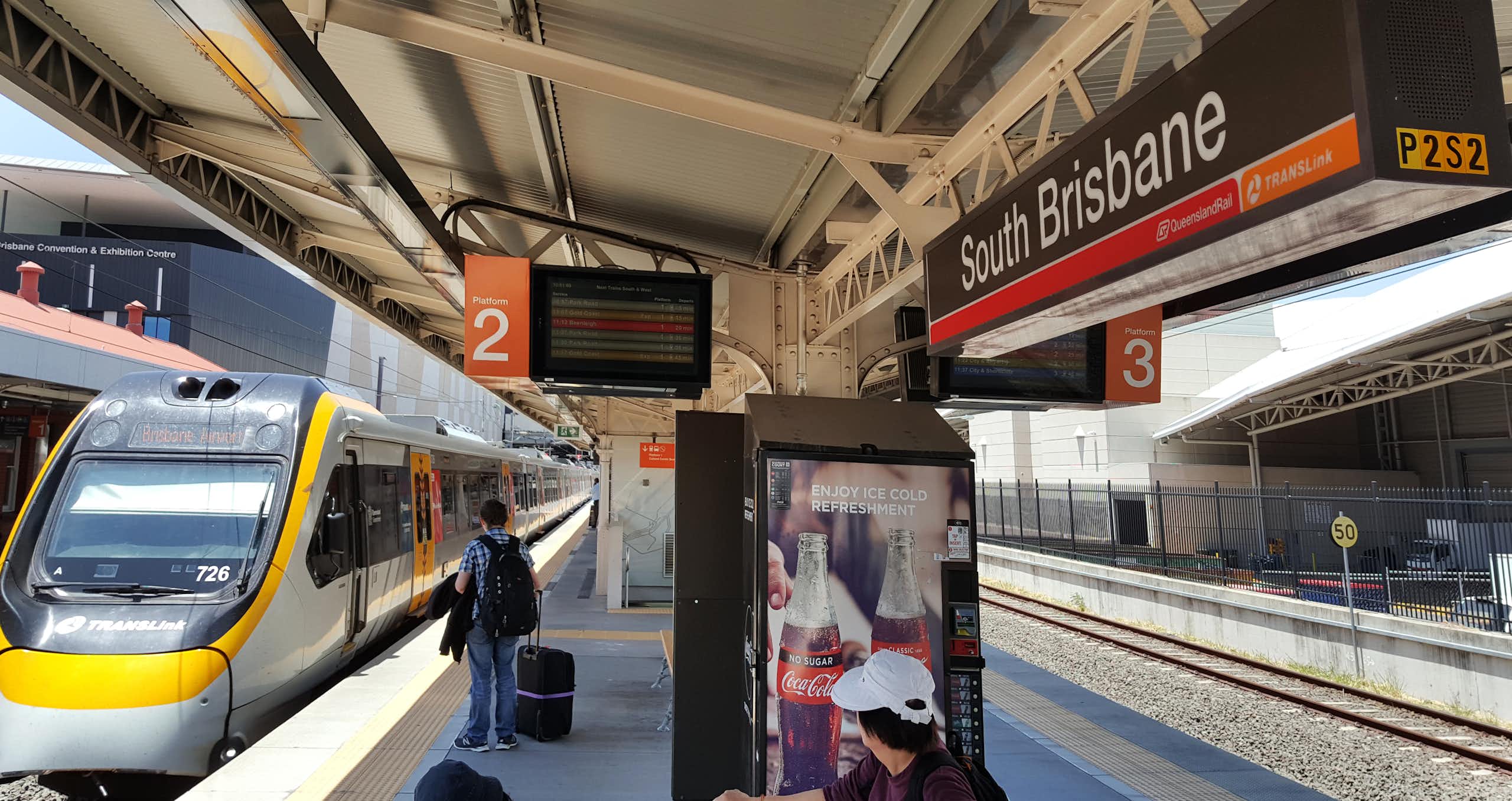 Train pulls into South Brisbane station, man seen waiting on platform with suitcase