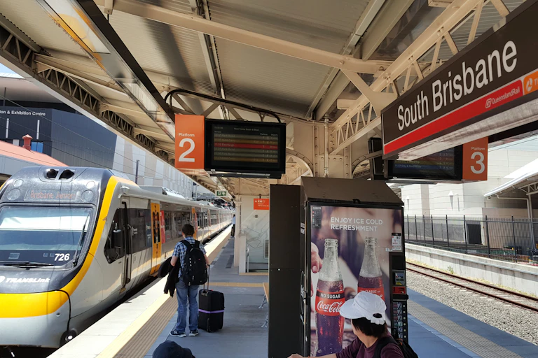 Train pulls into South Brisbane station, man seen waiting on platform with suitcase