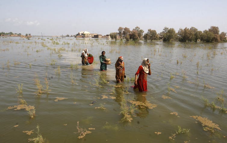 Four women wade through deep, vast floodwaters.