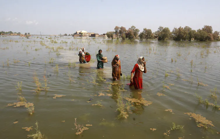 Four women wade through deep, vast floodwaters.