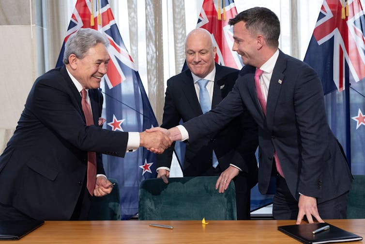 Winston Peters shakes hands with David Seymour as Christopher Luxon watches