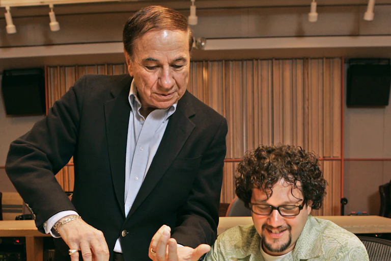 Two men look at sheet music, Sherman looks like he could be conducting.