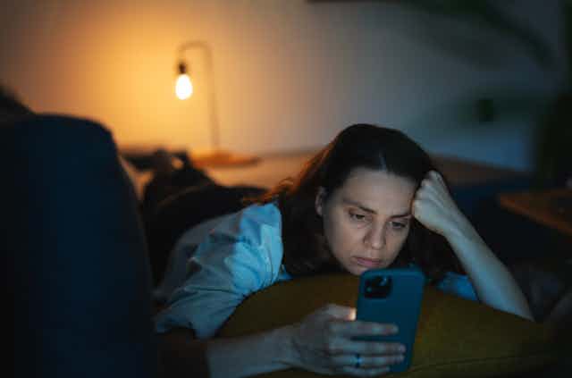 Photo of a woman lying down looking at her phone in a dark room 