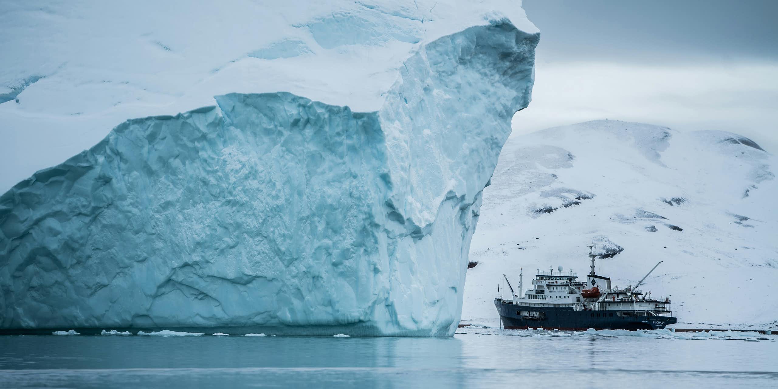 An iceberg dwarfs a fishing trawler, with Greenland in the background..
