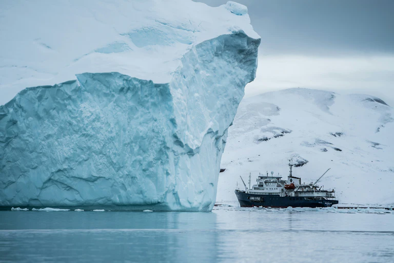 An iceberg dwarfs a fishing trawler, with Greenland in the background..