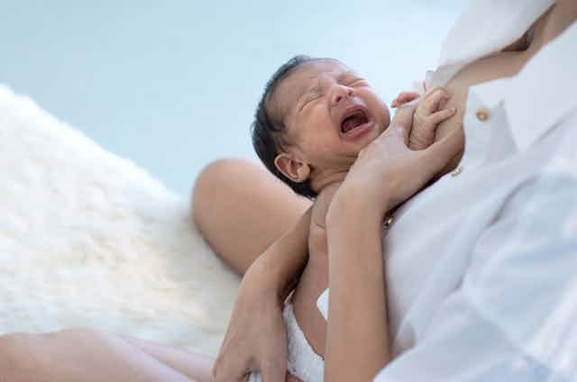 baby cries while mother holds it for breastfeeding