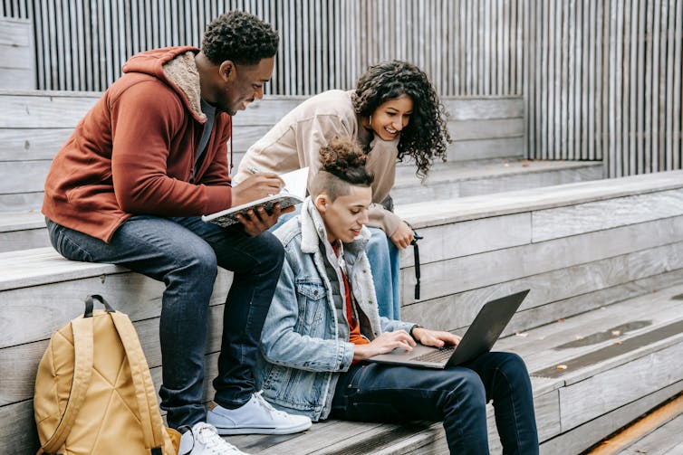 Three young people sitting on stairs looking at a laptop.