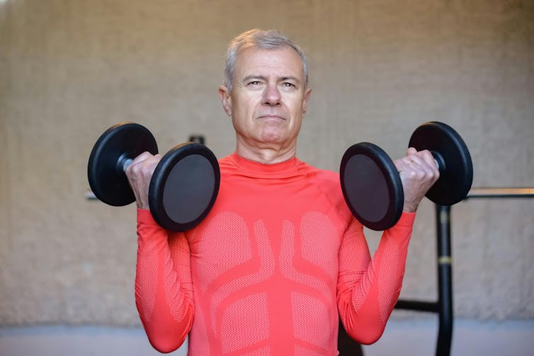 An older man does bicep curls in the gym