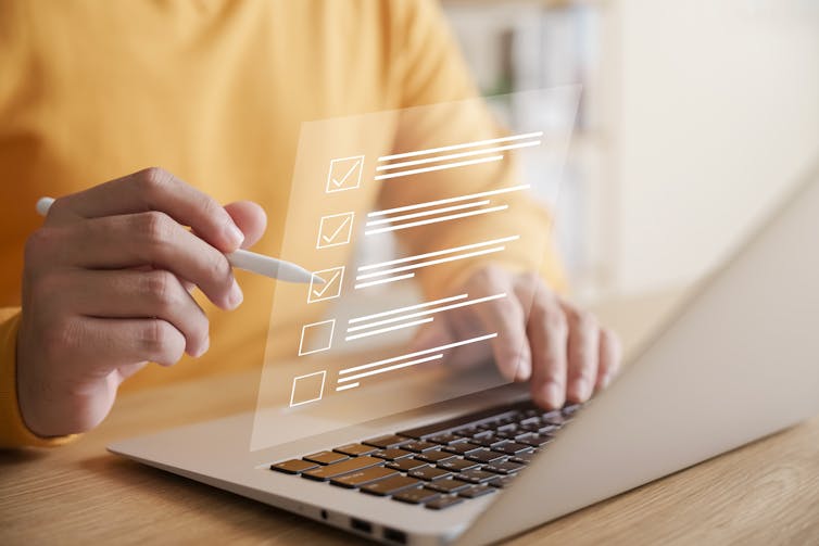 person ticks off list items that are pictured floating in air over laptop