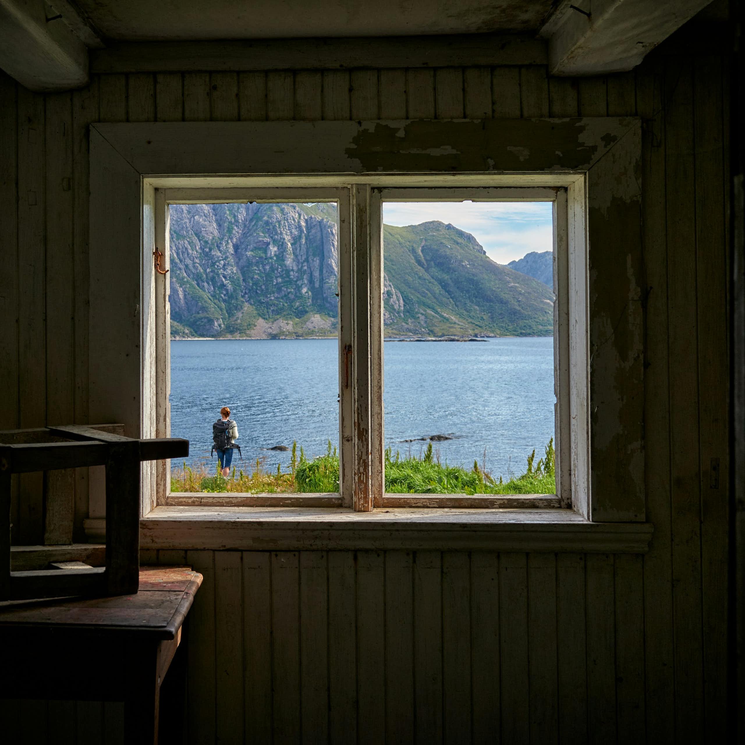 Une fenêtre dans un mur donne une vue sur un paysage lacustre.