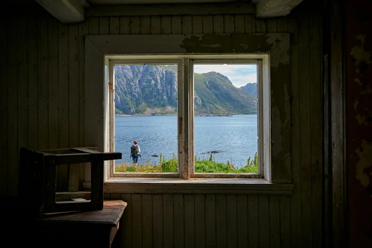 Une fenêtre dans un mur donne une vue sur un paysage lacustre.