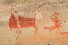 An ancient rock painting of humans hunting animals