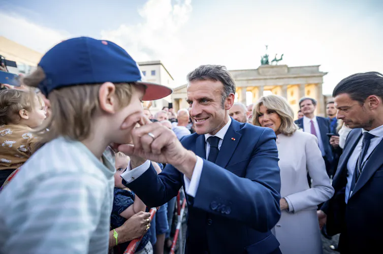 Le président français Emmanuel Macron et son épouse Brigitte Macron saluent les spectateurs après avoir franchi la porte de Brandebourg à Berlin, le 26 mai 2024, dans le cadre de la visite d’État du président français en Allemagn