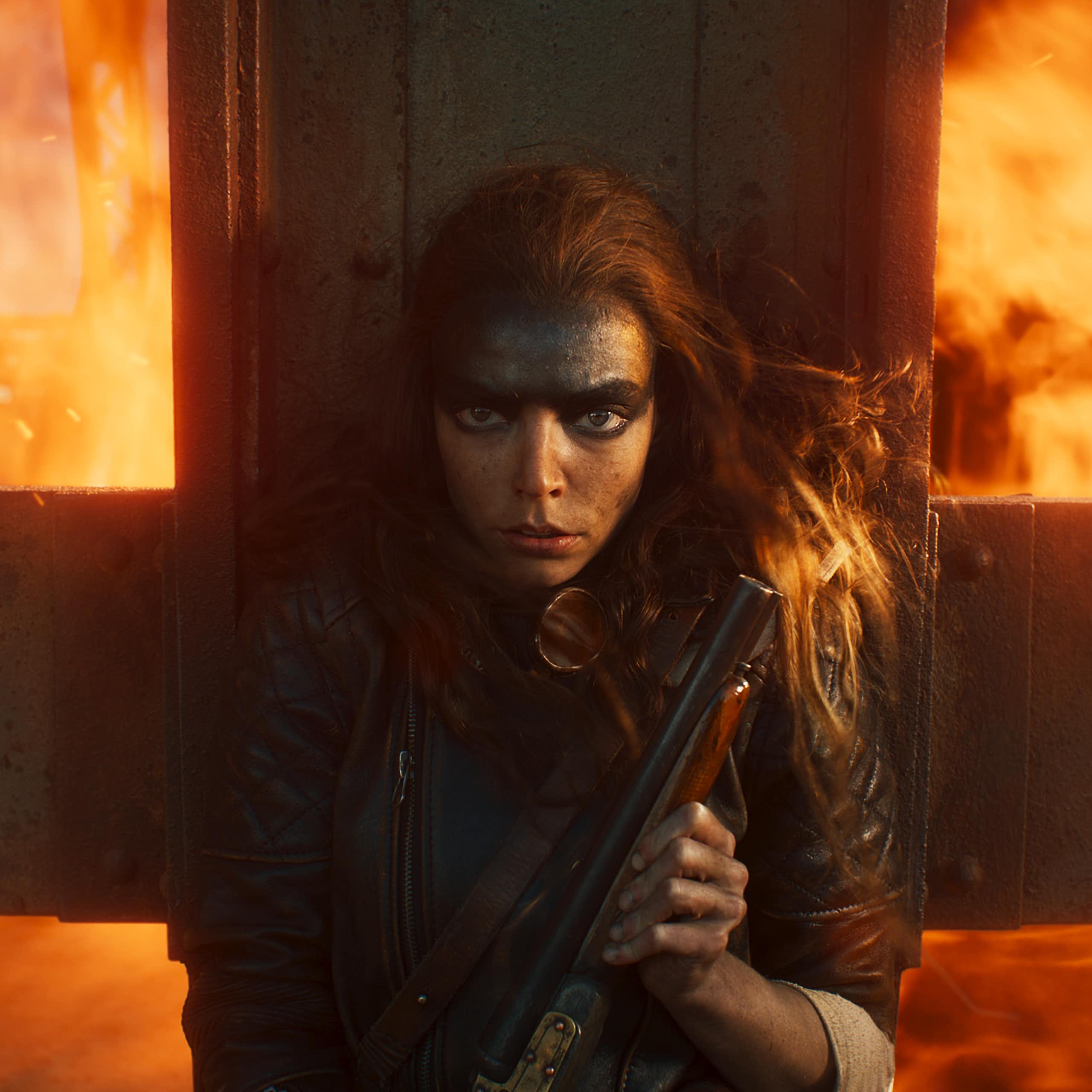 Anya Taylor-Joy holding a gun against a crucifix, fire blazing behind her.