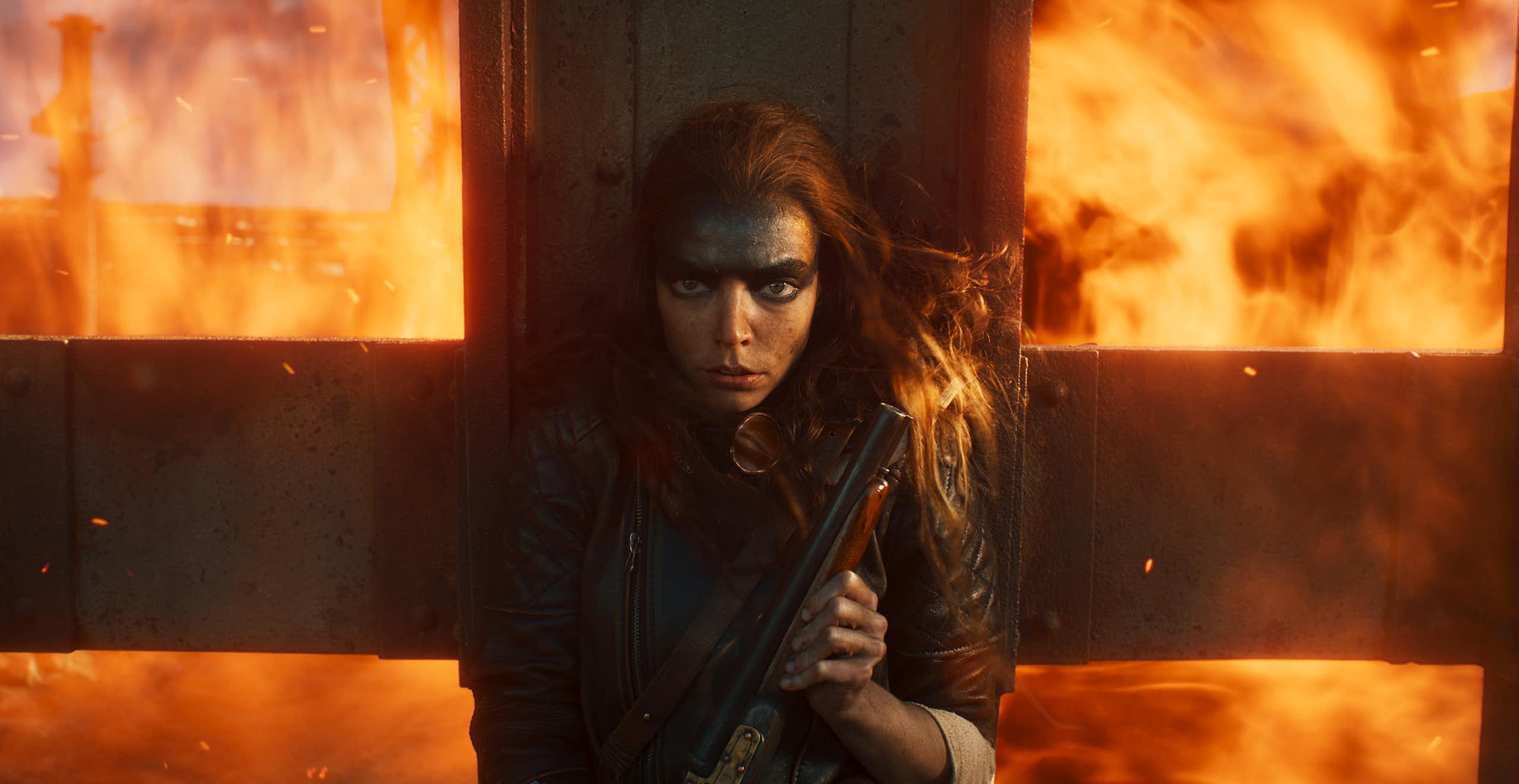 Anya Taylor-Joy holding a gun against a crucifix, fire blazing behind her.