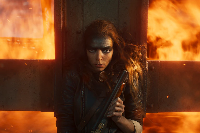 Anya Taylor-Joy holding a gun against a crucifix, fire blazing behind her.