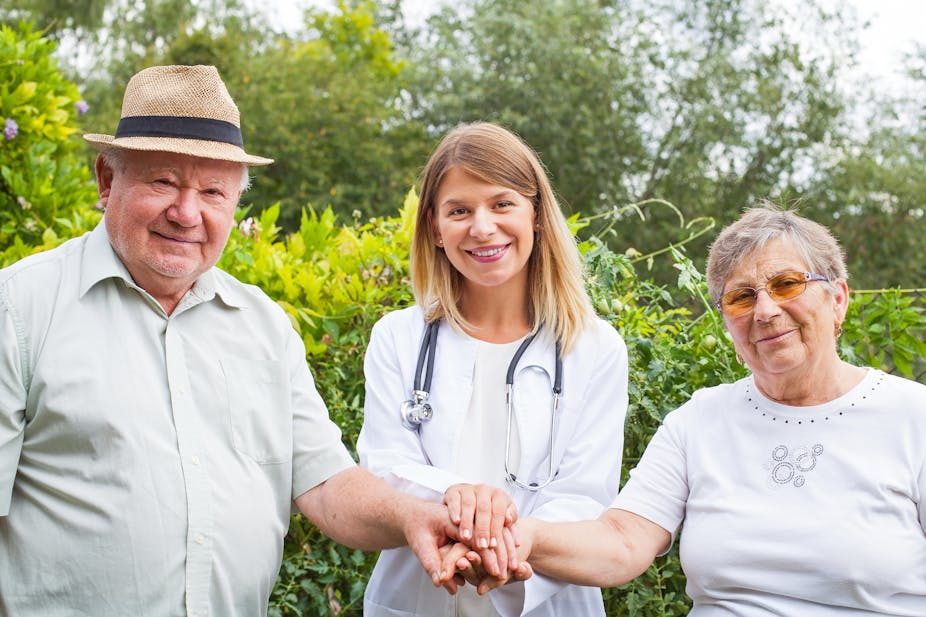 Une femme médecin souriante main dans la main avec un couple de personnes âgées en plein air
