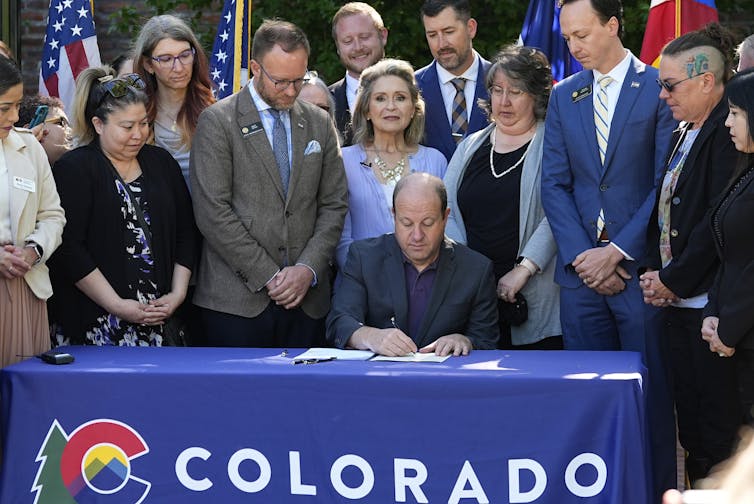 A man sits at a table signing a piece of paper.