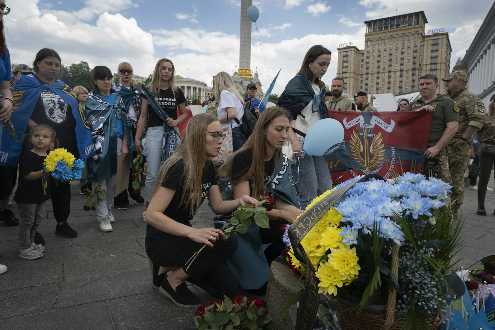 Des femmes déposent des fleurs au milieu d’une rue, entourée par une foule